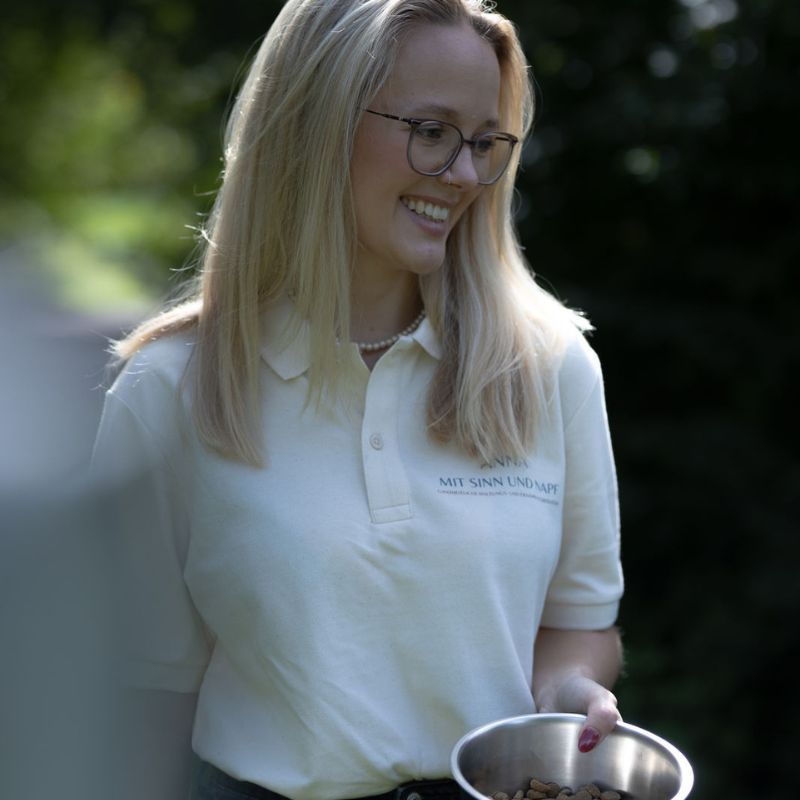 Anna Behnken von Mit Sinn und Napf hält einen Napf mit Trockenfutter in der Hand.